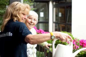 Ehrenamtlerin des DRK hilft einer Seniorin beim Blumengießen